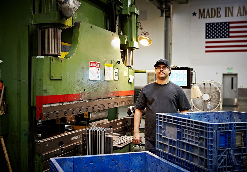 A man working in a machine shop with a USA flag on the wall